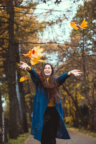 Playful young woman with autumn leaves in hand and fall yellow maple garden background