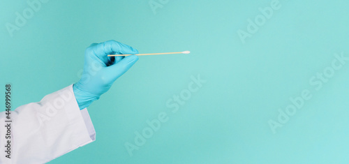 One Cotton stick for swab test in hand with blue medical gloves or latex glove on mint green or Tiffany Blue background.covid-19 concept. close up