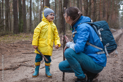Mom and child walk in the forest road after rain in raincoats together