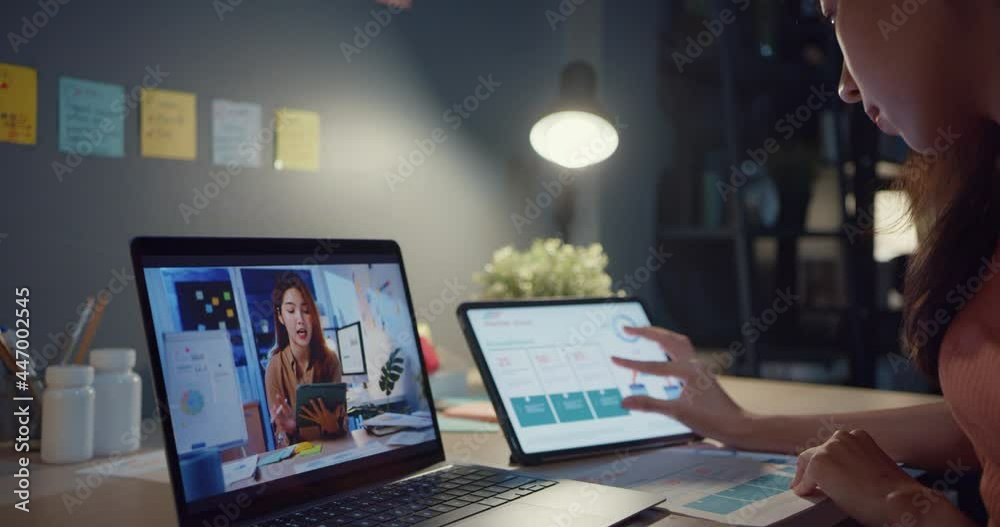 Asia woman using laptop talk to colleagues about work in video call while working from home at living room at night. Self-isolation, social distancing, quarantine for coronavirus prevention. Asia woman using laptop talk to colleagues about work in video call while working from home at living room at night. Self-isolation, social distancing, quarantine for coronavirus prevention.