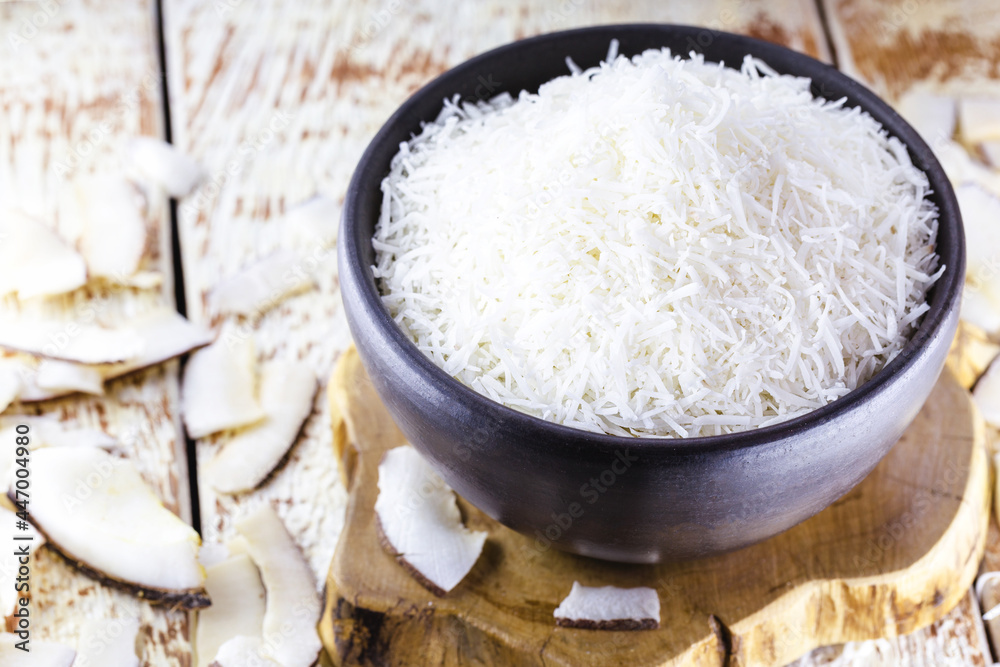 grated coconut inside a clay bowl, with coconut and coconut pieces in the background, culinary ingredient for sweets grated coconut inside a clay bowl, with coconut and coconut pieces in the background, culinary ingredient for sweets