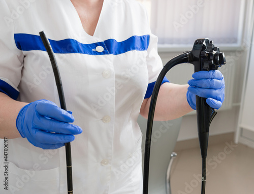A female doctor in white suit holds medical equipment for video esophagogastroduodenoscopy in her hands in blue gloves. Endoscopy Room