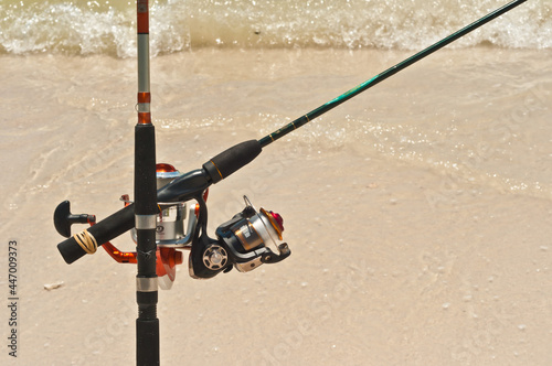 ront view, medium distance of two fishing poles in sand stand and connected, so one rod vertical and one rod horizontal, at a tropical shoreline