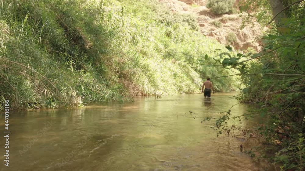 Man Walking On Shallow Water River Of Ayna Forest In Spain. - Sideways Shot Man Walking On Shallow Water River Of Ayna Forest In Spain. - Sideways Shot