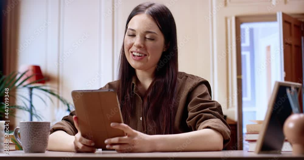 Hello. Brunette caucasian girl sitting at the armchair, looking at the tablet screen while having webcam conversation. Young woman speaking on video call using wireless internet connection at office Hello. Brunette caucasian girl sitting at the armchair, looking at the tablet screen while having webcam conversation. Young woman speaking on video call using wireless internet connection at office