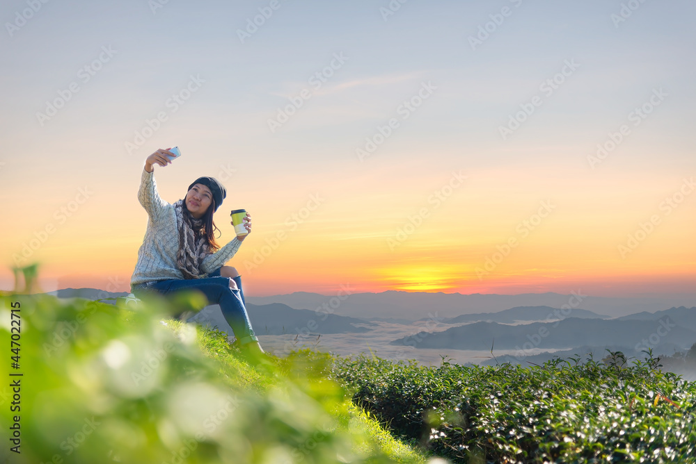 Asian women holding hot tea cup for drinking and take a photo in the morning day, relaxing and sitting outdoor in the tea plantation in sunshine light enjoying life her warm at balcony. Lifestyle Asian women holding hot tea cup for drinking and take a photo in the morning day, relaxing and sitting outdoor in the tea plantation in sunshine light enjoying life her warm at balcony. Lifestyle