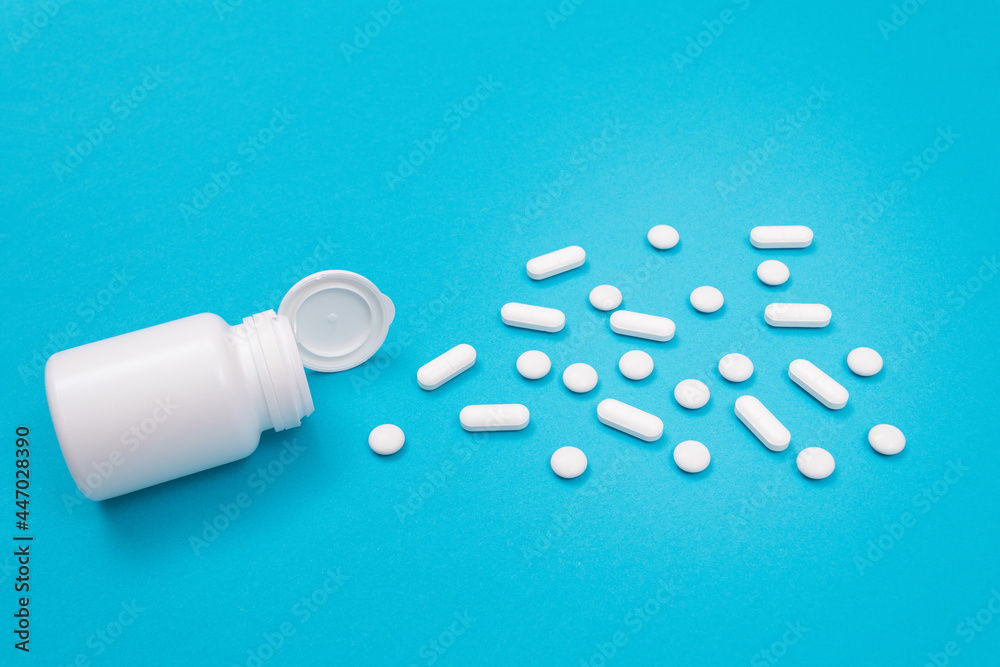Global Pharmaceutical Industry and Medicinal Products - White Pills or Tablets Scattered from the Pill Container, Lying on Blue Background Global Pharmaceutical Industry and Medicinal Products - White Pills or Tablets Scattered from the Pill Container, Lying on Blue Background