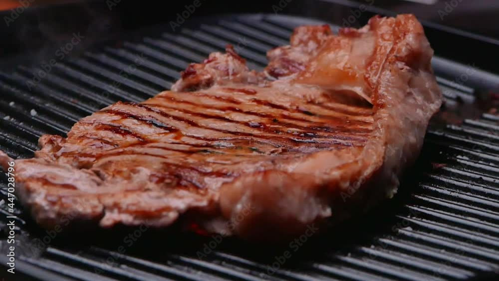 Roasting juicy meat steak with spices and herbs on a grill plate and smoke rised in slow motion. Healthy food concept. Roasting juicy meat steak with spices and herbs on a grill plate and smoke rised in slow motion. Healthy food concept.