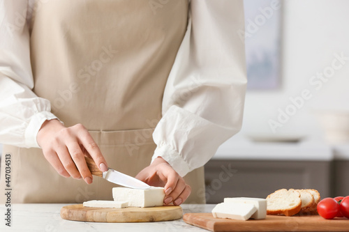Woman cutting delicious feta cheese on table