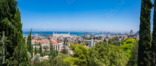 Panoramic view of Haifa - the red rooftops of the historic German Colony neighbourhood, the Haifa port and the blue waters of the Mediterranean Sea; framed on both sides by large cypress trees