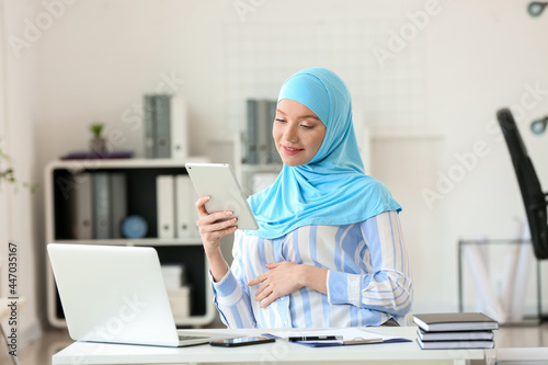Pregnant Muslim woman working with laptop in office