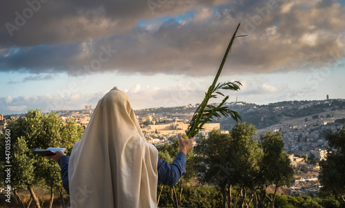 Succot (Feast of Tabernacles) in Jerusalem: Jewish man in a Tallit praying while waving the Four Species, with a view towards the Temple Mount, the Old City and the Mount of Olives