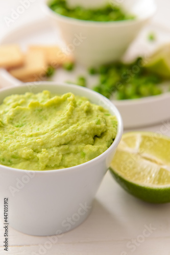 Bowl with tasty green pea hummus and lime on light background, closeup