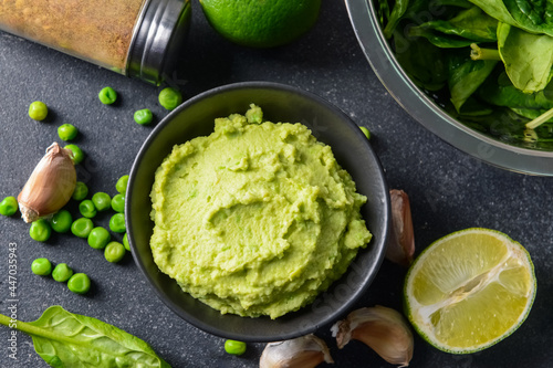 Fotografi Bowl with tasty green pea hummus, lime and garlic on dark background, closeup