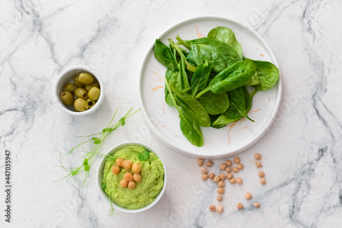 Bowl with tasty green pea hummus, olives and spinach on light background