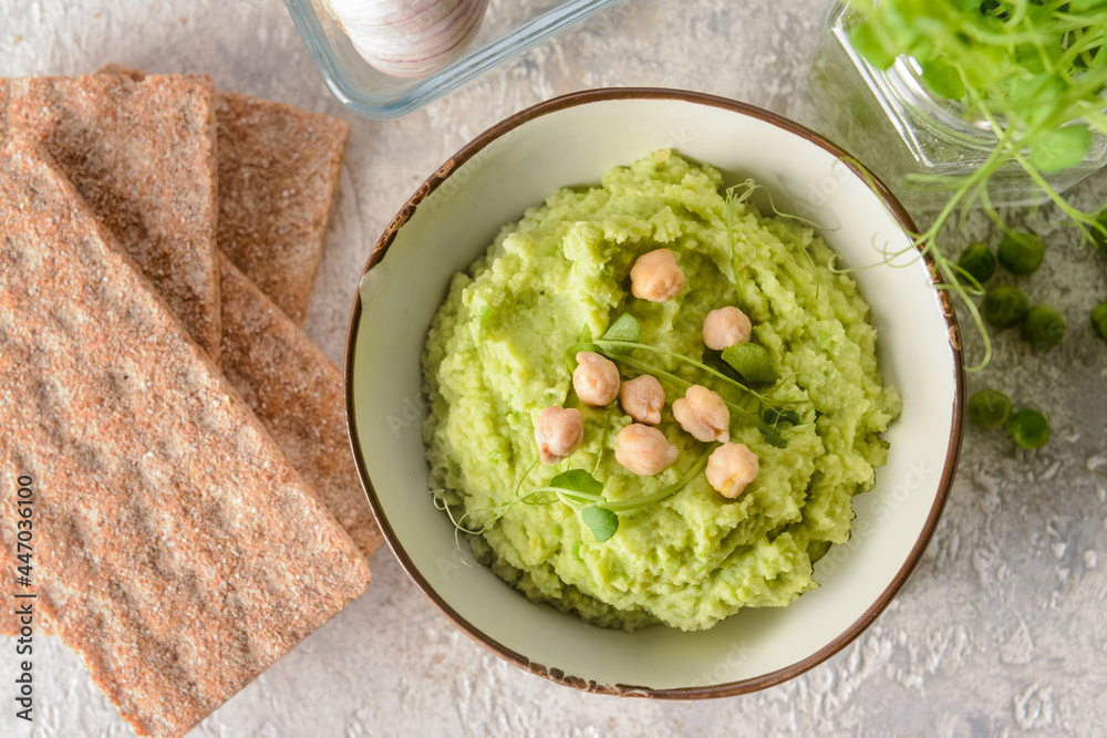 Bowl with tasty green pea hummus and crackers on light background, closeup Bowl with tasty green pea hummus and crackers on light background, closeup