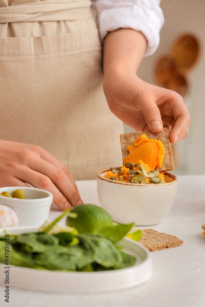 Woman with tasty carrot hummus and cracker on light table, closeup Woman with tasty carrot hummus and cracker on light table, closeup
