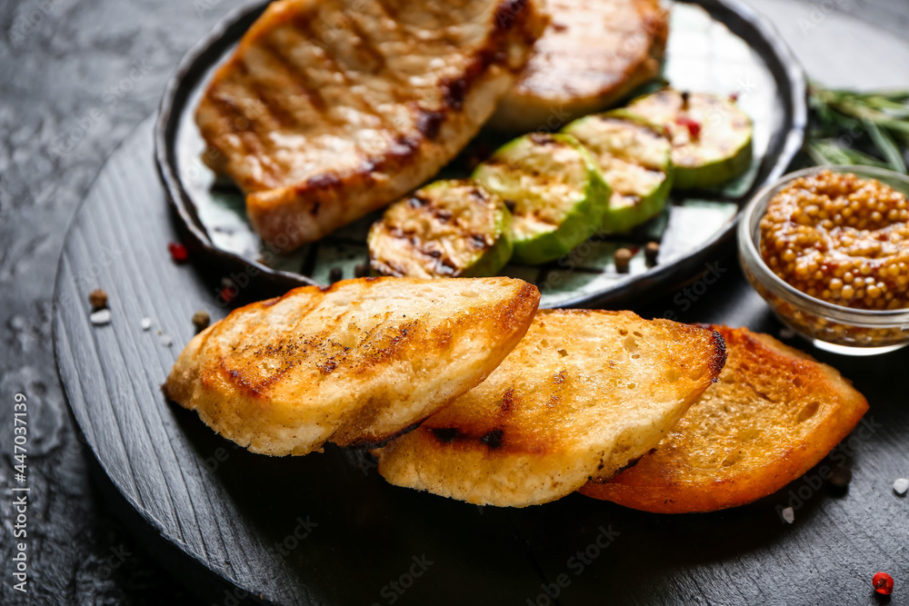 Board with tasty grilled bread and steaks on dark background Board with tasty grilled bread and steaks on dark background