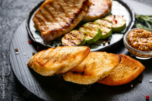 Board with tasty grilled bread and steaks on dark background