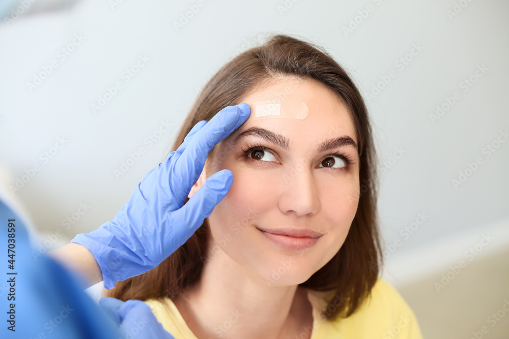Nurse applying medical patch on young woman's forehead in clinic Nurse applying medical patch on young woman's forehead in clinic