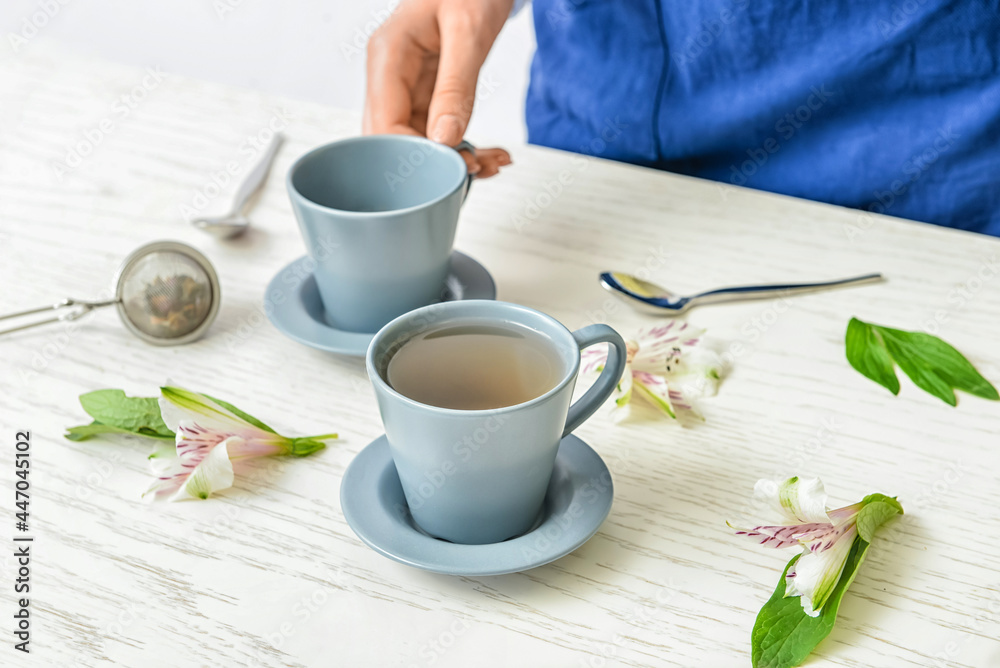 Woman with cups of floral tea on table Woman with cups of floral tea on table