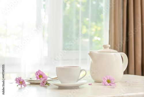 Cup of floral tea, teapot and flowers on table in room