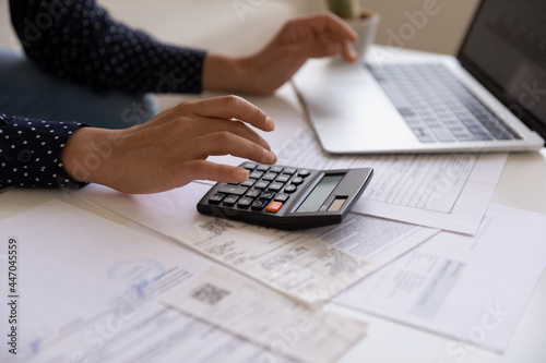 Close up cropped of Indian woman calculating and paying bills online, using calculator and laptop at home, young female planning budget, managing expenses, finances, checking internet banking service photo