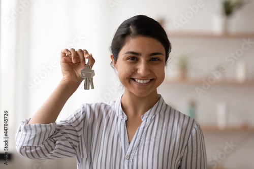Head shot portrait of smiling Indian woman showing keys, looking at camera, happy young female tenant renter satisfied buyer client excited by relocation, proud homeowner purchasing new apartment