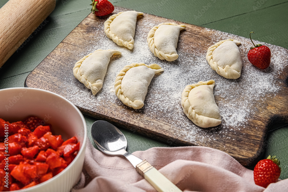Fototapeta premium Composition with raw dumplings and strawberry on color wooden background
