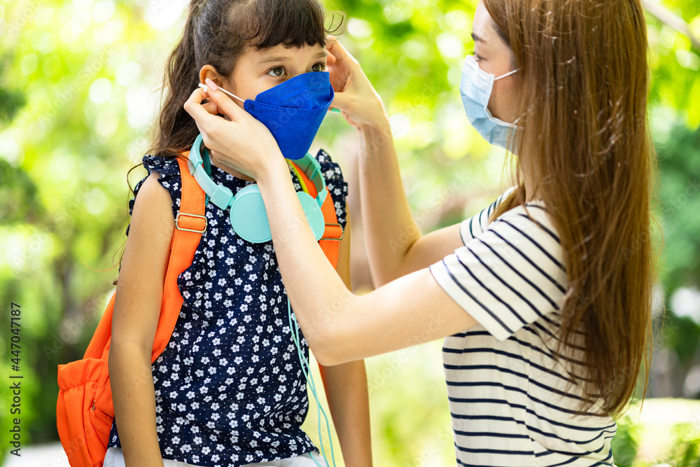 Mixed race mother preparing her little kid for the return to school wearing a mask. Back to school concept.Life during covid-19 pandemic. .Mother puts a safety mask on her daughter's face. Mixed race mother preparing her little kid for the return to school wearing a mask. Back to school concept.Life during covid-19 pandemic. .Mother puts a safety mask on her daughter's face.