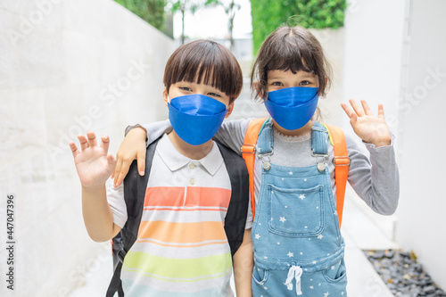 Little sister and brother in protective masks with school backpacks .View Of Elementary School Students Who Are Carrying A School Bag.
