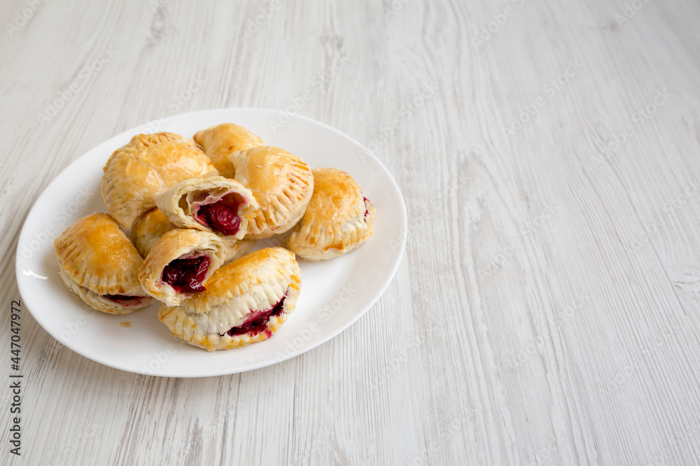 Homemade Cherry Hand Pies on a plate on a white wooden background, side view. Copy space. Homemade Cherry Hand Pies on a plate on a white wooden background, side view. Copy space.