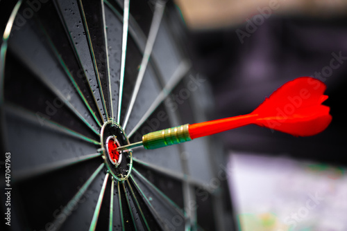 Close up shot of the dart arrow hit on bulleyes of dartboard to represent that the business reached the target of company with dark tone picture style. Target and goal as concept.