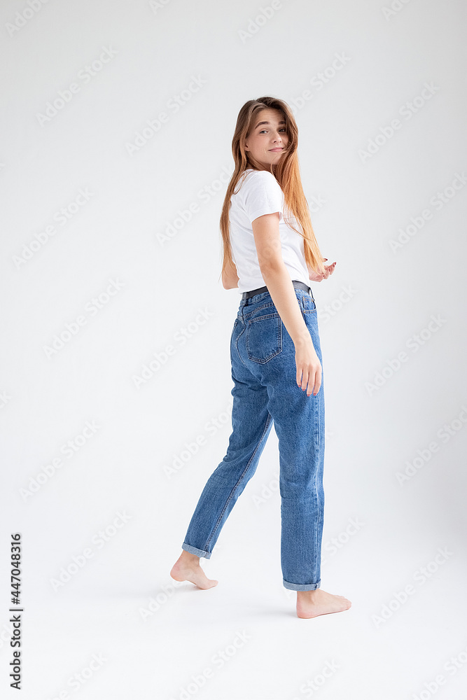young attractive caucasian woman with long hair in t-shirt and blue jeans isolated on white studio background. skinny pretty female posing on cyclorama with bare feet. model tests of beautiful lady young attractive caucasian woman with long hair in t-shirt and blue jeans isolated on white studio background. skinny pretty female posing on cyclorama with bare feet. model tests of beautiful lady