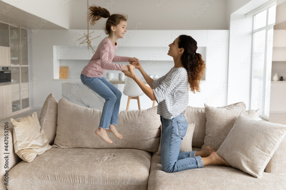 Overjoyed Latino mom and small teen daughter have fun jump on couch in living room on leisure weekend. Smiling Hispanic mother and teenage girl child relax rest at home, feel playful crazy together. Overjoyed Latino mom and small teen daughter have fun jump on couch in living room on leisure weekend. Smiling Hispanic mother and teenage girl child relax rest at home, feel playful crazy together.