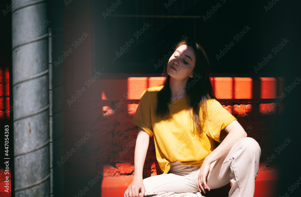 Portrait of a young happy trendy modern brunette woman in a yellow t-shirt on a background of red shadow with shadow in face Portrait of a young happy trendy modern brunette woman in a yellow t-shirt on a background of red shadow with shadow in face