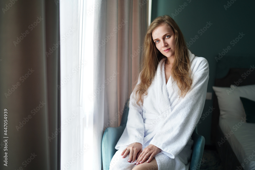 Young beautiful girl near window, resting in the hotel room in the morning. Positive good mood, restoration of health, renewal of the nervous system. Long hair is down. Cute face with natural makeup. Young beautiful girl near window, resting in the hotel room in the morning. Positive good mood, restoration of health, renewal of the nervous system. Long hair is down. Cute face with natural makeup.