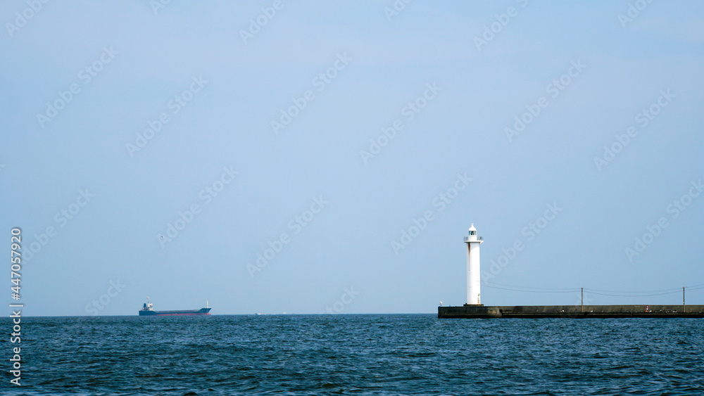 東京湾に突き出た防波堤の上に立つ白い灯台と遠くに見えるタンカー
