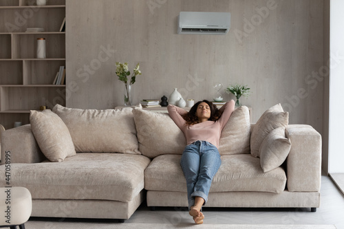 Calm millennial Latino woman lying relaxing on couch in living room breathe fresh ventilated condition air. Happy young Hispanic female renter rest on sofa at home relieve negative emotions.
