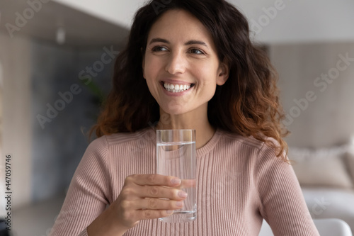 Close up of smiling millennial Latin woman hold glass drink clean pure still mineral water for body refreshment. Happy young Hispanic female enjoy clear aqua feel thirsty. Hydration concept.