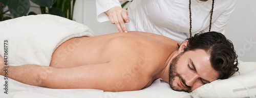 Male patient with acupuncture needles inserted in his back is receiving treatment chronic back pain in a traditional Chinese medicine clinic with acupuncturist