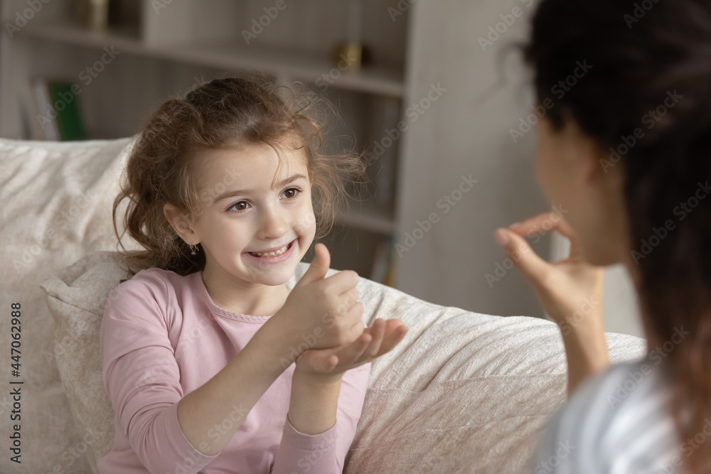 Small ethnic girl child make hand gesture talk with mom use sign language. Smiling little biracial numb deaf disabled kid communicate with tutor or coach. Disability, nonverbal communication concept. Small ethnic girl child make hand gesture talk with mom use sign language. Smiling little biracial numb deaf disabled kid communicate with tutor or coach. Disability, nonverbal communication concept.