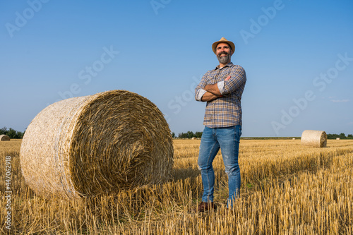 Happy farmer is standing beside bales of hay. He is satisfied because of successful harvesting.