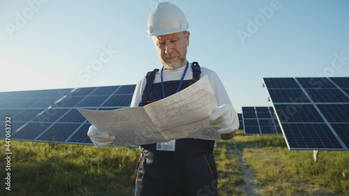 Adult engineer on modern solar power plant checking work standing across the batteries on green sunny summer field. Futuristic technology innovation. Ecology and environment. Eco-friendly system