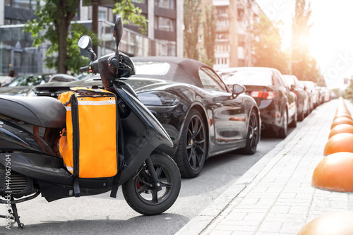 Photography Fast express takeaway online gig order food delivery scooter with red orange bag box parked at traffic city center downtown street on sunny day
