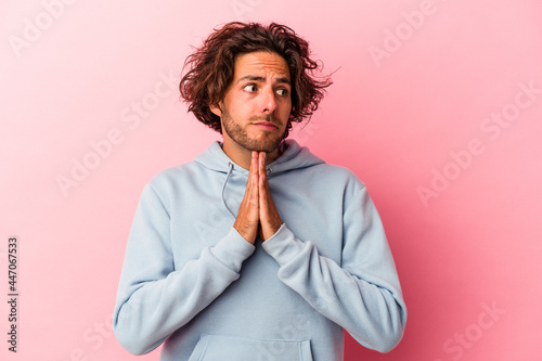Young caucasian man isolated on pink bakcground praying, showing devotion, religious person looking for divine inspiration.