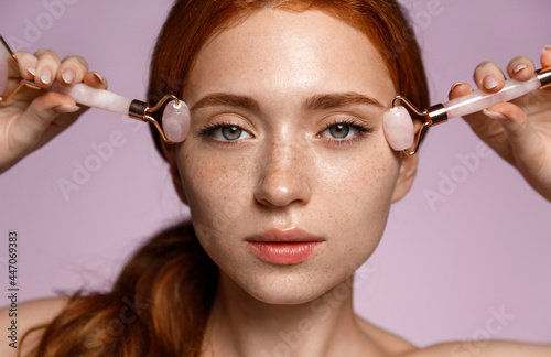 Close up of redhead girl, with clean perfect skin, using skincare massage jade rollers, cosmetic procedure to reduce wrinkles, anti-aging cosmetology and spa concept