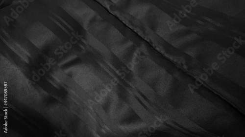 close up dark black satiny blanket or silky fabric background with beautiful creased pattern. crumpled black silk bed sheet background. close up black velvet of rippled fabric. © WONGSAKORN