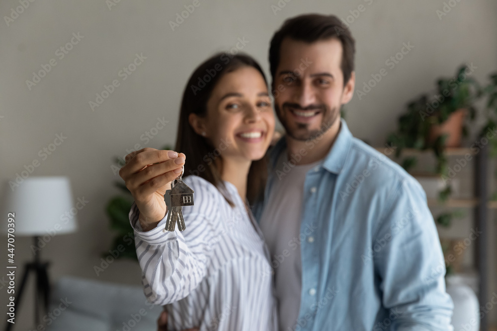 Happy married 30s couple smile look at camera, close up focus to keys bunch from newly bought house. Bank mortgage for young family, start new independent life at own home, housing improvement concept Happy married 30s couple smile look at camera, close up focus to keys bunch from newly bought house. Bank mortgage for young family, start new independent life at own home, housing improvement concept