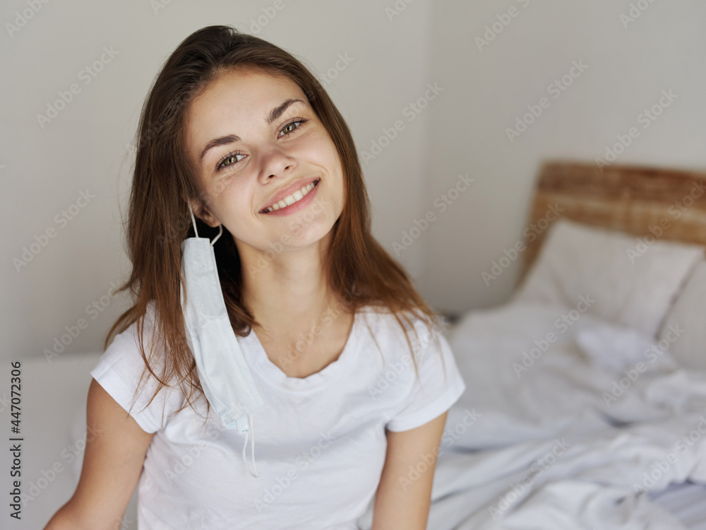 young woman wearing a medical mask sitting on the bed smile health model young woman wearing a medical mask sitting on the bed smile health model